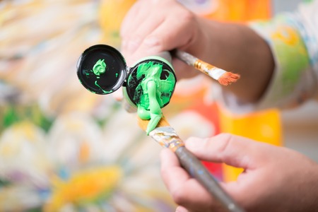 Selected focus on the brush with green paint on it in the hands of the brilliant painter standing...