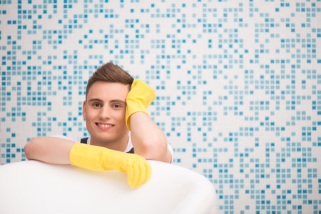 Half-length portrait of young dark-haired smiling janitor wearing white T-shirt blue overalls and...