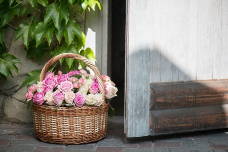 Very nice basket with violet roses standing on the threshold at the door of ivied little wooden houseの写真素材