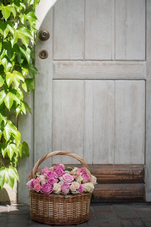 Very nice basket with violet roses standing on the threshold at the door of ivied little wooden houseの写真素材
