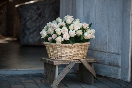 Wonderful basket with white roses standing on the little wooden stool in the wooden houseの写真素材
