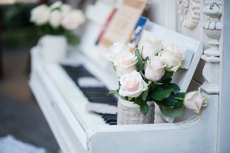 Selective focus on beautiful little bouquet of white roses standing in the nice decorated cup on the white splendid piano on backgroundの写真素材