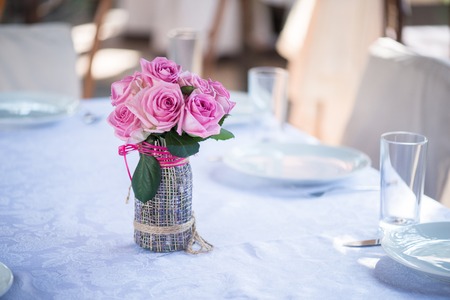 Selective focus on the great decorated glass with violet roses in it standing on the elegant table with coversの写真素材