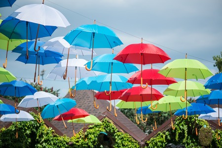 Beautiful street with many green trees on it decorated with nice colored umbrellas hanging over the...