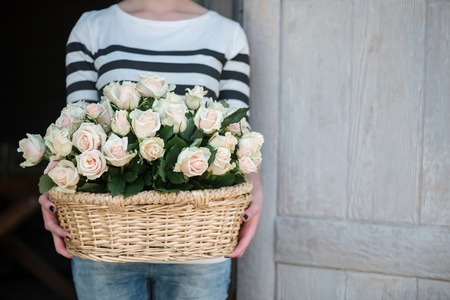 Woman wearing nice jersey and blue jeans coming out the house with nice twisted basket of white rosesの写真素材