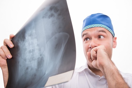 Half-length portrait of very surprised surgeon wearing white shirt and blue cap looking at the roentgenograph. Isolated on white backgroundの写真素材