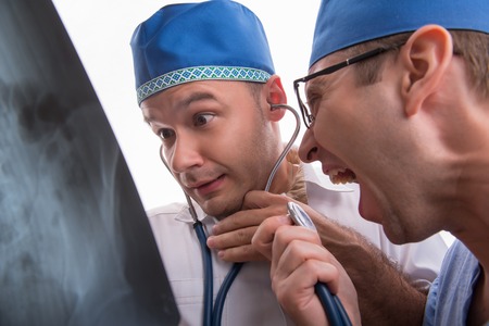 Half-length portrait of two excited doctors wearing blue caps one of them keeping a stethoscope and another says something in it looking at the radiograph astonished. Isolated on white backgroundの写真素材
