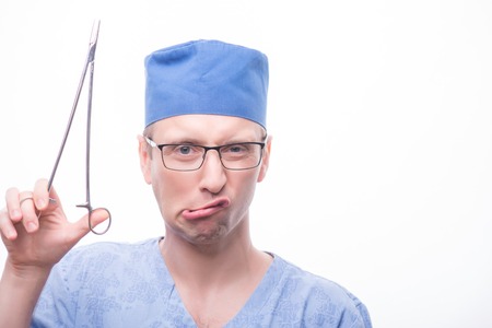 Half-length portrait of funny surgeon wearing eyeglasses blue cap and medical dress holding a pair of scissors. Isolated on white backgroundの写真素材