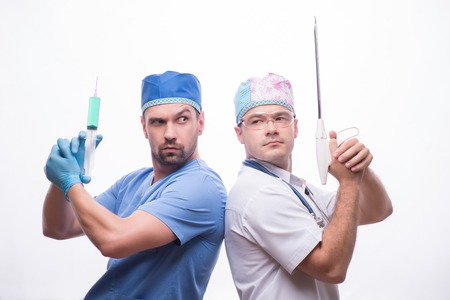 Half-length portrait of two funny doctors wearing medical dress standing back to each other holding injector and medical apparatus like weapon. Isolated on white background の写真素材