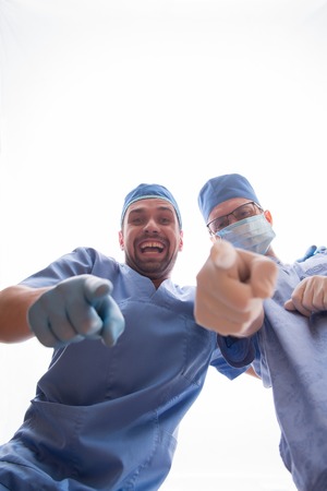 Half-length portrait of two smiling doctors wearing medical dress pointing at us. Isolated on white backgroundの写真素材