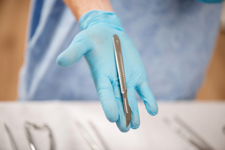 Selective focus on the scalpel lying on the palm of the doctor wearing blue disposable glovesの写真素材