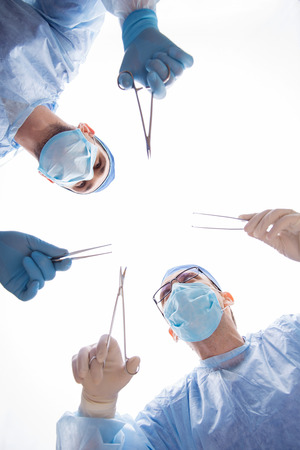 Half-length portrait of two doctors wearing blue medical masks and uniform holding a pair of scissors and tweezers in both hands operating the patient looking at each other. Low angle の写真素材