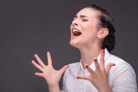Half-length portrait of dark-haired angry beautiful woman wearing white blouse standing aside...