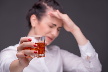Selective focus on the glass of whisky in the hands of dark-haired tired beautiful woman wearing...