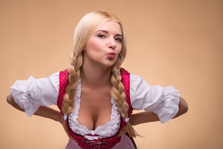 Half-length portrait of young sexy smiling blonde wearing pink dirndl with white blouse leaning to us showing her breast. Isolated on dark backgroundの写真素材