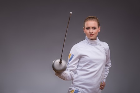 Half-length portrait of pretty smiling girl wearing fencing costume practicing in fencing with her rapier. の写真素材