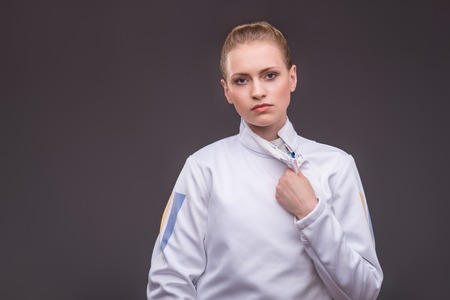 Half-length portrait of pretty tired girl unbuckling her white fencing costume. の写真素材