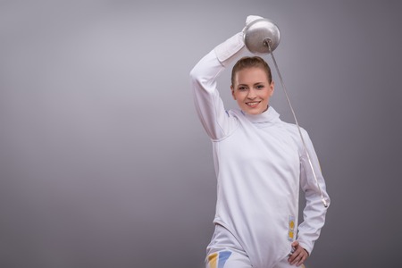 Half-length portrait of pretty smiling girl wearing fencing costume practicing in fencing with her rapier.の写真素材