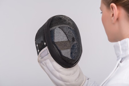 Half-length portrait of pretty girl wearing fencing costume looking straight at her black fencing...