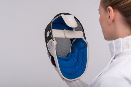 Half-length portrait of pretty girl wearing fencing costume looking straight at her blue fencing mask. Isolated on white backgroundの写真素材