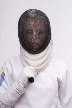 Half-length portrait of woman wearing white fencing costume and black wanted to take off her fencing mask looking at us. Isolated on white backgroundの写真素材