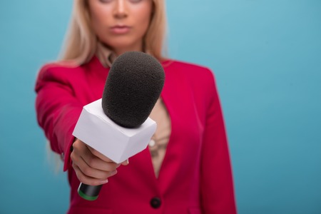 Selective focus on the microphone in the hands of the TV presenter wearing great red jacket and cream-colored shirt standing on backgroundの写真素材