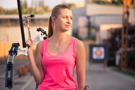 Selective focus on the lovely young fair-haired woman wearing pink T-shirt and black skirt holding the bow with arrows looking out for someoneの写真素材