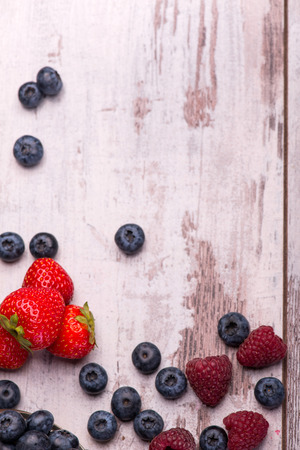 Still life with the tempting raspberry lying near the scattering blackberry and red delicious strawberry on the wooden table. Top viewの写真素材