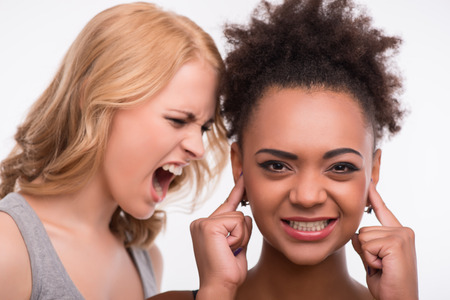 Half-length portrait of young pretty blonde standing aside screaming at her smiling friend. Isolated on white backgroundの写真素材