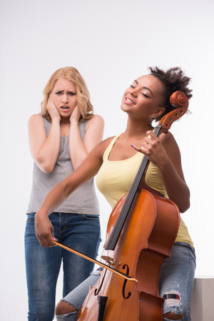 Half-length portrait of lovely dark-haired girl wearing yellow T-shirt and jeans playing on the violin and poor blonde cannot put up with this noise. Isolated on white backgroundの写真素材