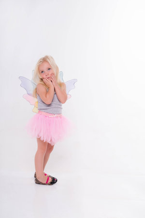 Full-length portrait of little fair-haired lovely girl wearing pretty grey vest and rose skirt standing aside with white wings looking at us. Isolated on white backgroundの写真素材