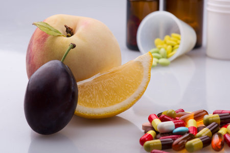 Selective focus on the tempting peach slice of orange and plum lying on the white surface. Heap of colorful pills on backgroundの写真素材