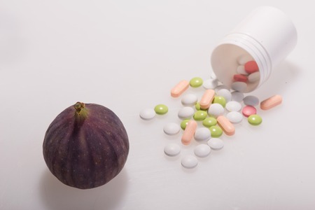 Tempting fig lying near the heap of colorful pills. Concept of health in pills and fruitsの写真素材