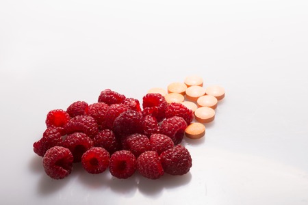Very delicious raspberry lying near the tablets on the white surface. Concept of health in pills and fruitsの写真素材