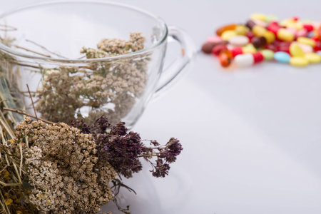 Selective focus on the glass cup with some herbs in it standing near the heap of colorful pills on background. Concept of healthy lifeの写真素材