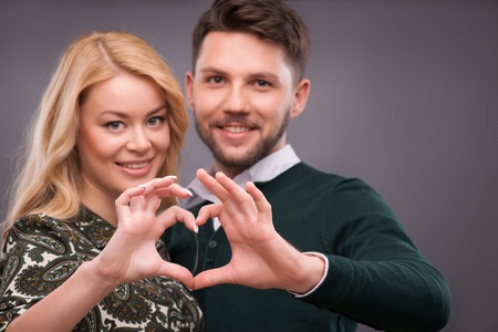 Selective focus on the hands making a form of little heart. Lovely smiling couple standing on backgroundの写真素材