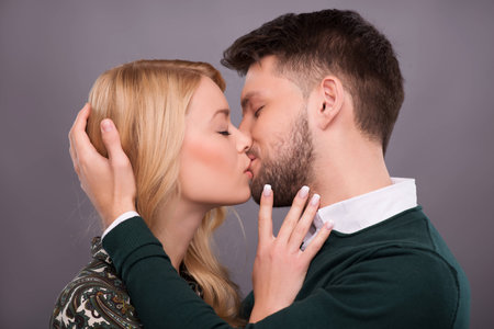 Half-length portrait of young beautiful couple standing with closed eyes facing each other kissing. Isolated on dark backgroundの写真素材