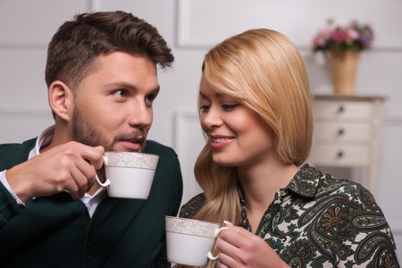 Selective focus on the lovely couple sitting together talking about their new family life drinking tea laughing looking at each otherの写真素材