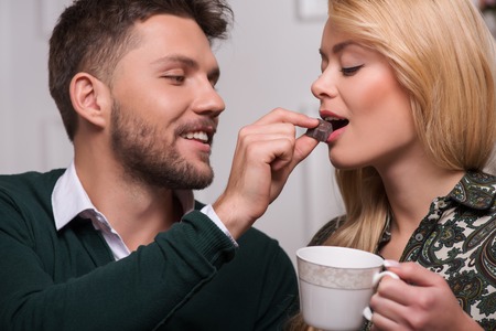 Selective focus on the lovely couple sitting together talking about something feeding each other with chocolate praline and laughingの写真素材