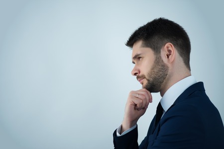 Half-length portrait of handsome young bearded thoughtful man wearing white shirt tie and blue jacket standing aside wanted to remember something. Isolated on white backgroundの写真素材