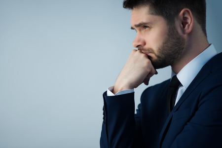 Half-length portrait of handsome young bearded thoughtful man wearing white shirt tie and blue jacket standing aside wanted to remember something. Isolated on white backgroundの写真素材