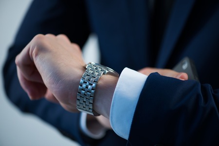 Selective focus on the watch on the hand of busy man wearing white shirt tie and blue jacketの写真素材