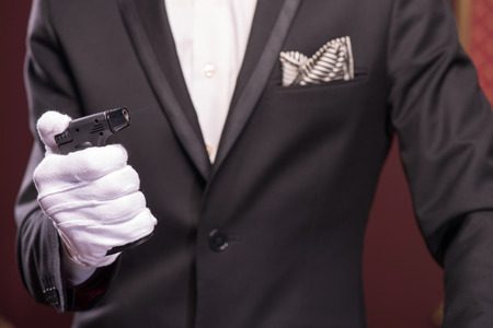 Selective focus on the hands of young aristocrat wearing costly black official costume and white gloves holding a cigar lighterの写真素材