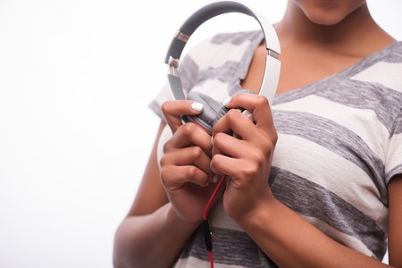 Selective focus on the lovely white earphones in the hands of smiling African girl wearing striped T-shirtの写真素材
