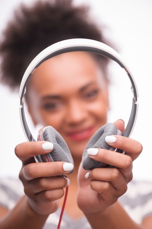Selective focus on the lovely white earphones in the hands of smiling African girl wearing striped T-shirtの写真素材