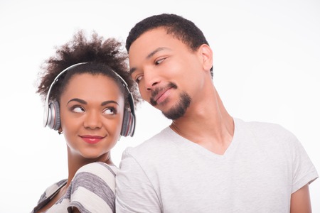 Half-length portrait of young smiling African woman keeping earphones on her head standing near her boyfriend looking at us contentedly. Isolated on white backgroundの写真素材