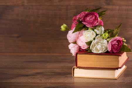 Selective focus on the pile of books with the flowers on the top of it lying on the wooden surfaceの写真素材