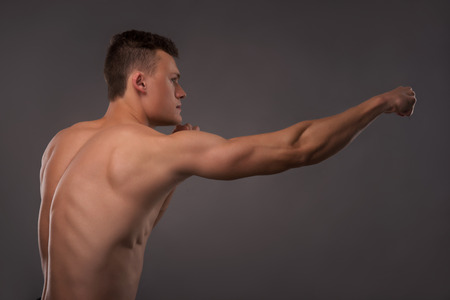 Half-length portrait of young handsome fair-haired bare-chested karate enthusiast standing aside training himself before the important fight. Isolated on the dark backgroundの写真素材