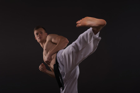 Half-length portrait of young handsome fair-haired bare-chested karate enthusiast standing training his strike before the important competition. Isolated on the dark backgroundの写真素材