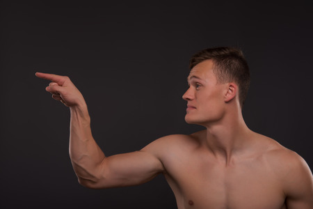 Half-length portrait of young handsome fair-haired bare-chested karate enthusiast standing aside asking someone to take his challenge. Isolated on the dark backgroundの写真素材